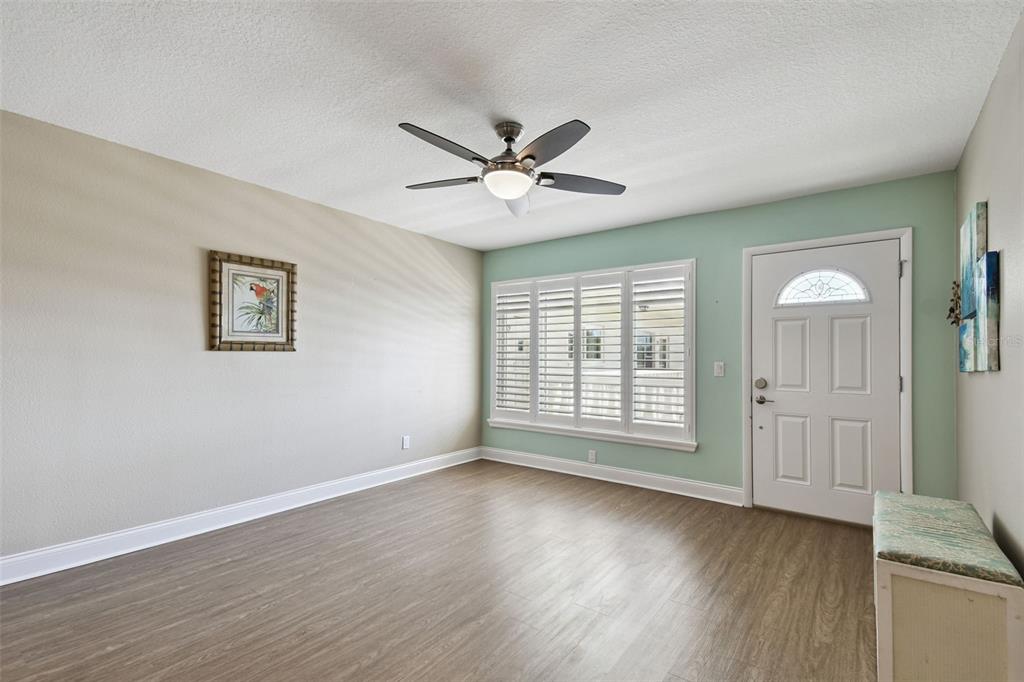 An empty room features wood-look flooring, a ceiling fan, plantation shutters, and a front door — 2292 COSTA RICAN DRIVE UNIT 30, CLEARWATER, FL