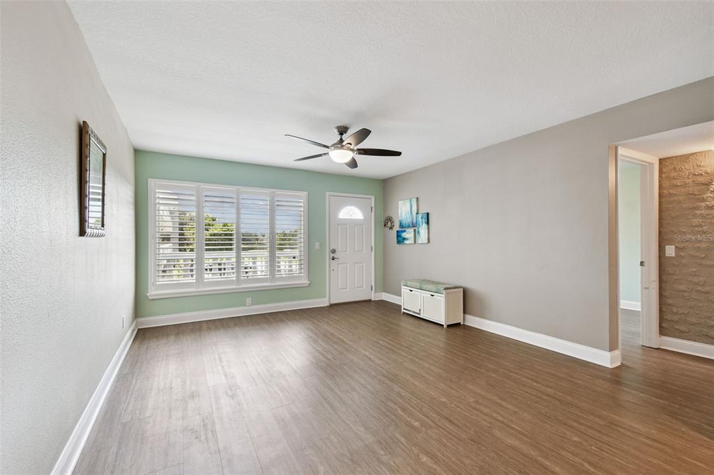 A living room features light-colored walls, wood-look flooring, a ceiling fan, and plantation shutters — 2292 COSTA RICAN DRIVE UNIT 30, CLEARWATER, FL