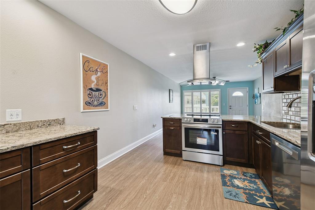 A kitchen features dark wood cabinets, granite countertops, stainless steel appliances, and light wood flooring — 2292 COSTA RICAN DRIVE UNIT 30, CLEARWATER, FL