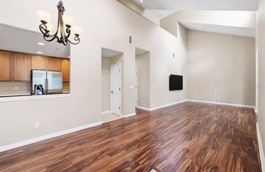 A spacious living room with high ceilings, wood-look flooring, and an open kitchen pass-through — 316 NAUTICA MILE DRIVE, CLERMONT, FL