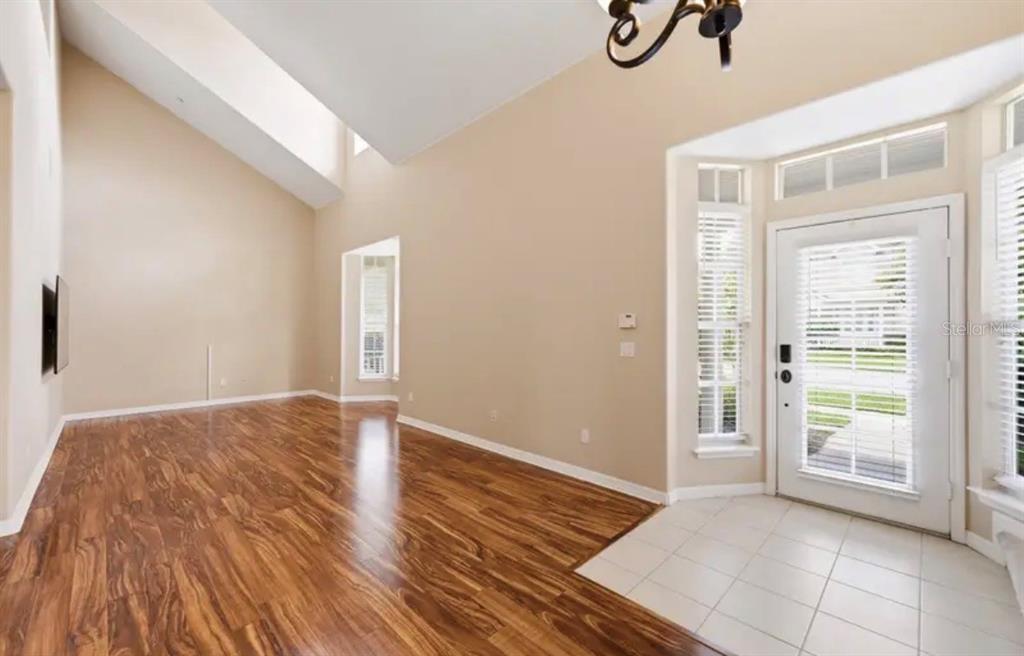 A living room with a high vaulted ceiling, dark sofa, two armchairs, and wood flooring — 316 NAUTICA MILE DRIVE, CLERMONT, FL
