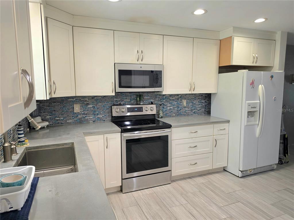 A kitchen features white cabinets, stainless steel appliances, a blue mosaic backsplash, and concrete countertops — 6777 WINKLER ROAD UNIT A236, FORT MYERS, FL