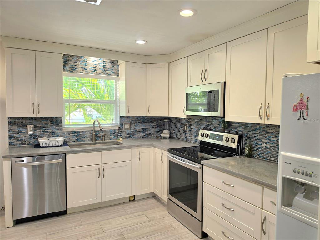 A kitchen features white cabinets, stainless steel appliances, gray countertops, and a blue mosaic backsplash — 6777 WINKLER ROAD UNIT A236, FORT MYERS, FL