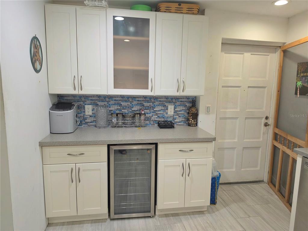 A kitchen wet bar features white cabinets, a glass-front beverage cooler, and blue tile backsplash — 6777 WINKLER ROAD UNIT A236, FORT MYERS, FL