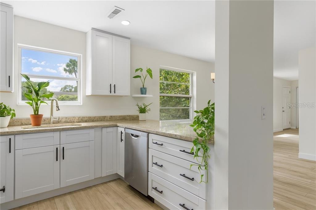 A modern kitchen features white cabinets, granite countertops, stainless steel appliances, and light wood flooring — 38 VISTA GARDENS TRAIL UNIT 207, VERO BEACH, FL