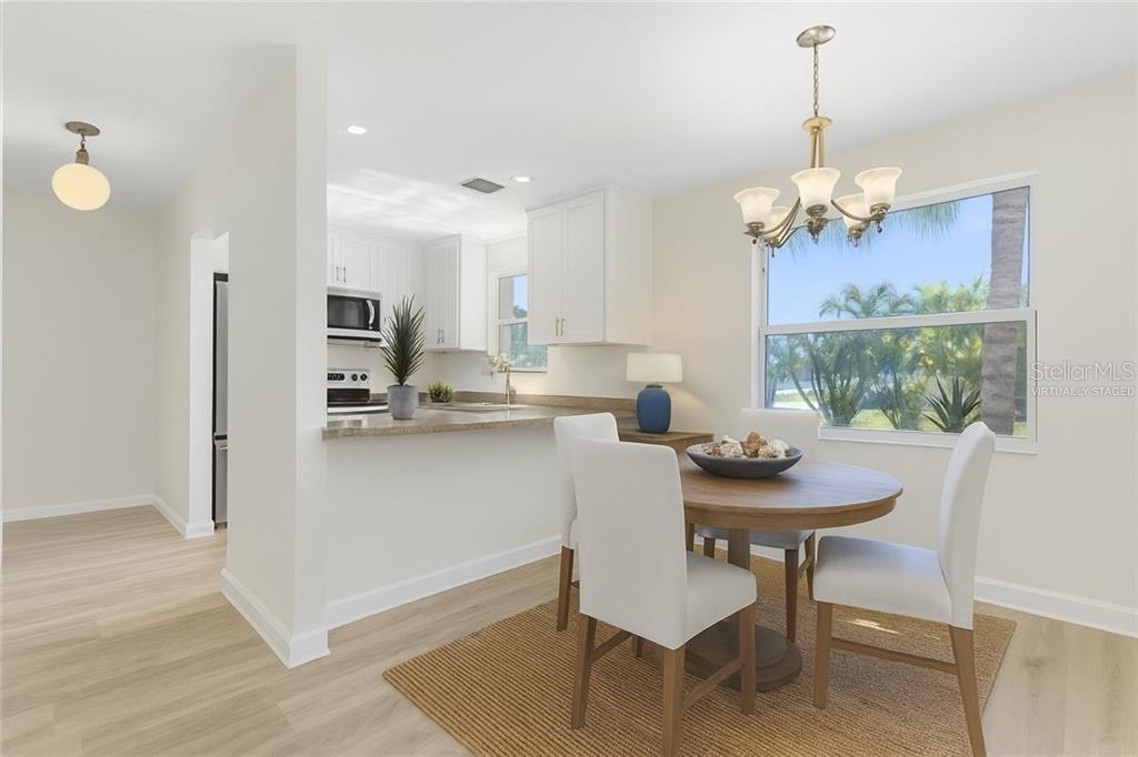 This virtually staged dining area features a round wooden table, white chairs, and kitchen access — 38 VISTA GARDENS TRAIL UNIT 207, VERO BEACH, FL