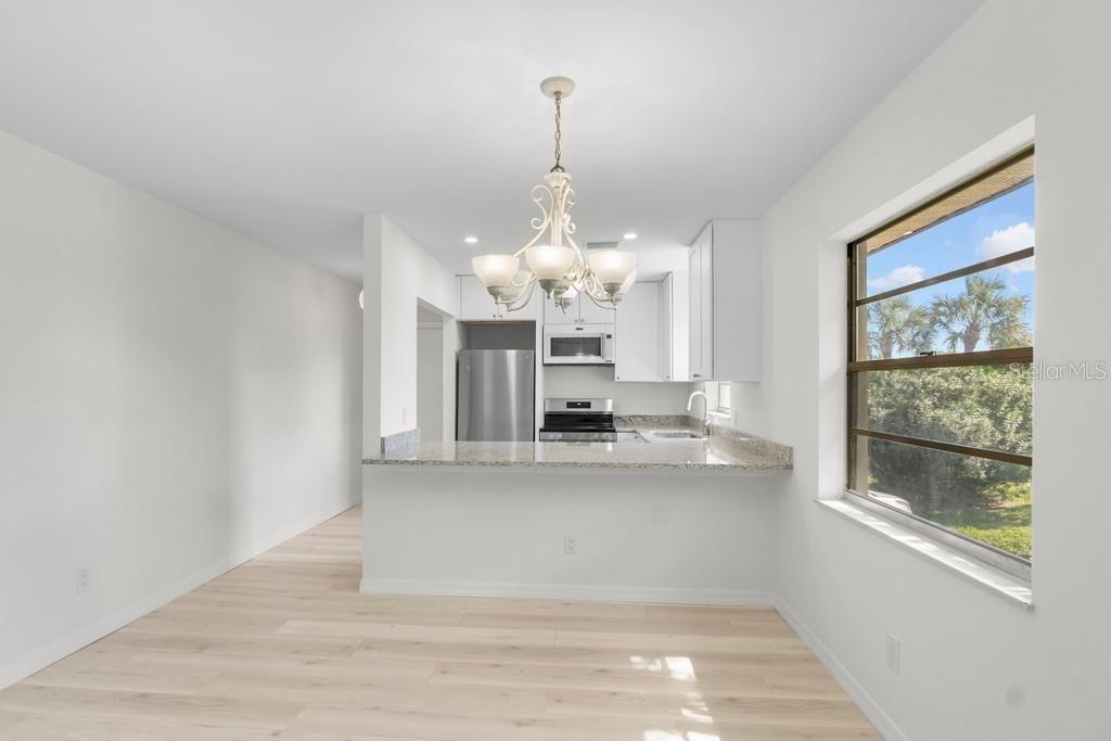 A bright dining area with light wood floors overlooks a kitchen with white cabinets — 38 VISTA GARDENS TRAIL UNIT 207, VERO BEACH, FL
