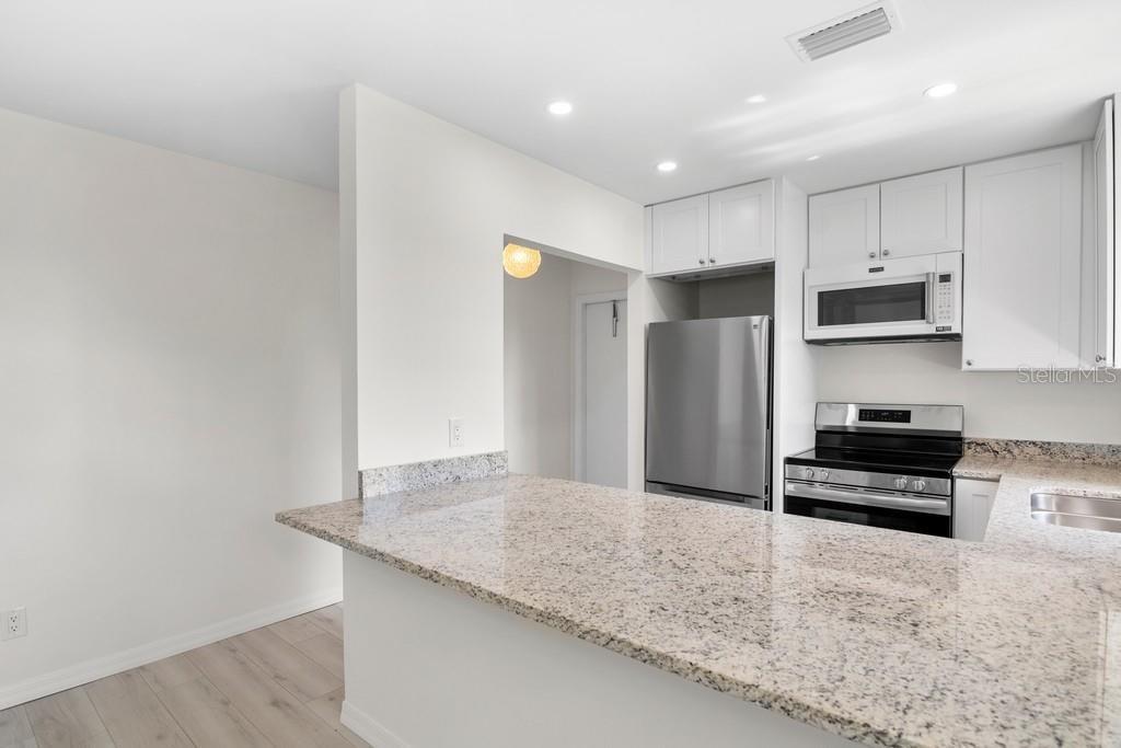 A kitchen features white cabinets, stainless steel appliances, and a granite breakfast bar countertop — 38 VISTA GARDENS TRAIL UNIT 207, VERO BEACH, FL