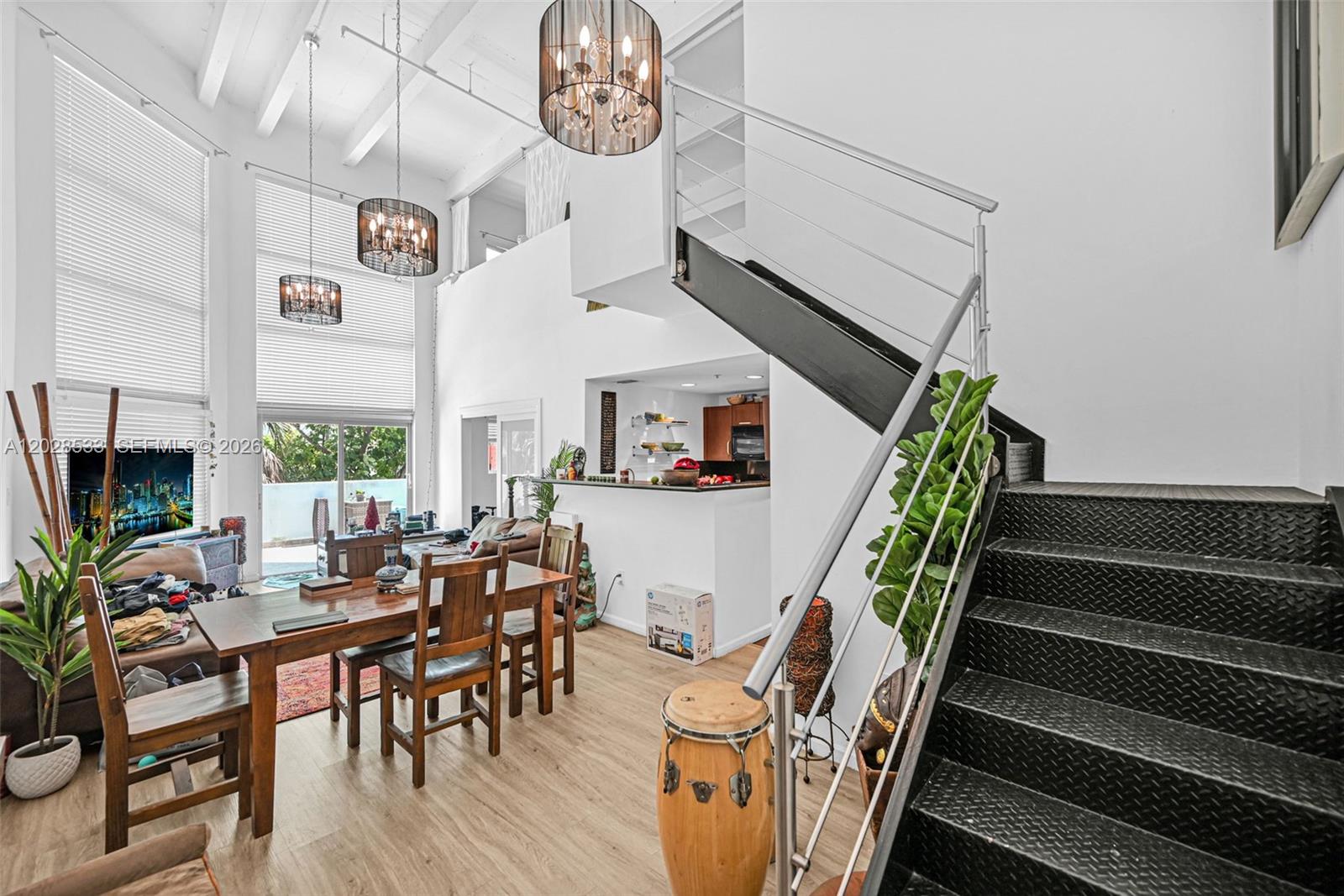 A high-ceilinged living and dining area features a metal staircase and modern light fixtures — 7728 Collins Ave # 5, Miami Beach FL 33141, MIAMI BEACH, FL