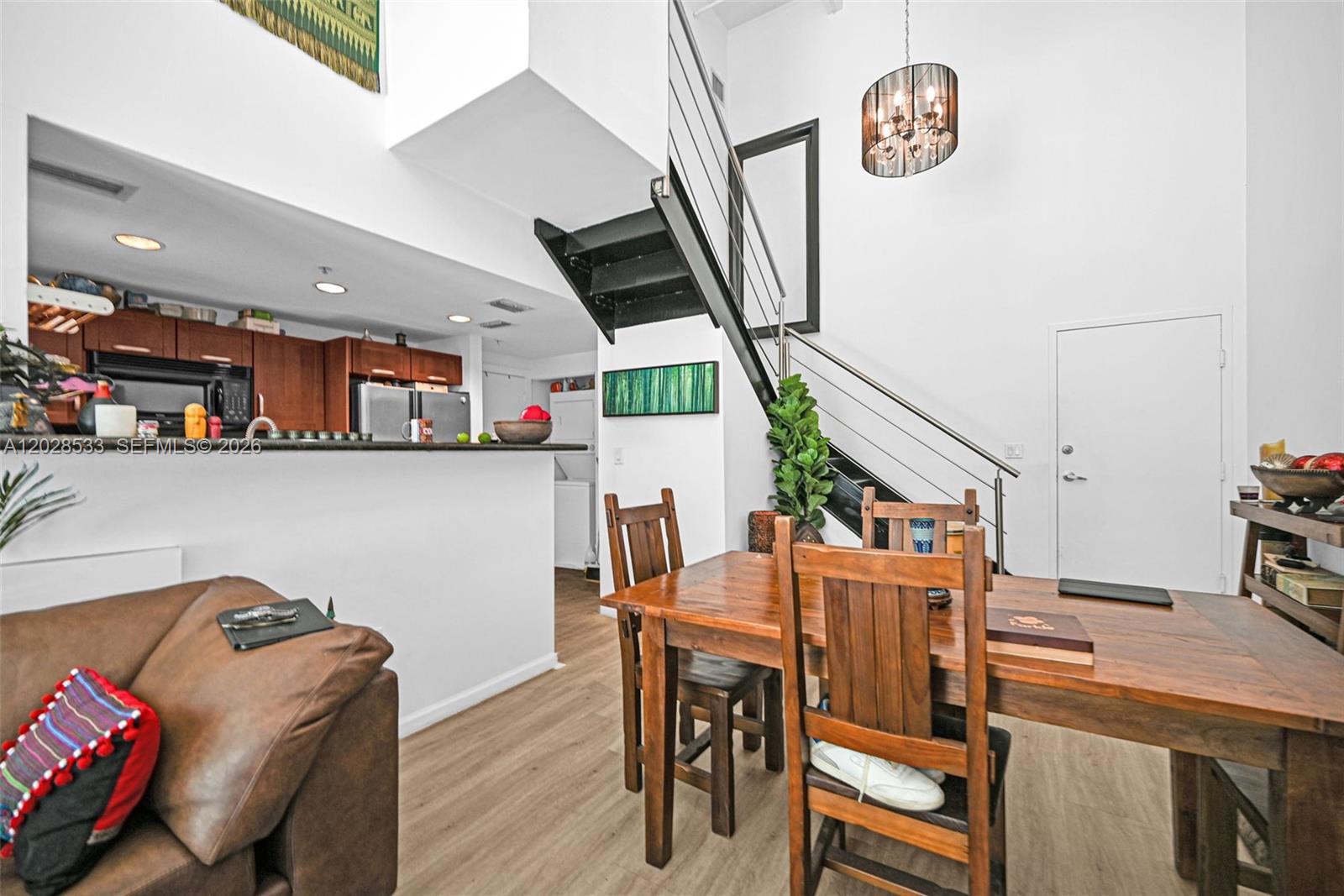 A dining area with a wooden table and chairs sits beside a staircase and kitchen — 7728 Collins Ave # 5, Miami Beach FL 33141, MIAMI BEACH, FL