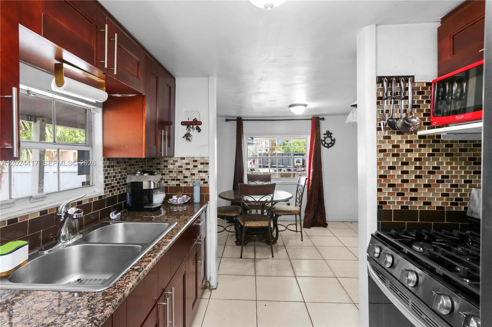 A kitchen with dark wood cabinets, granite countertops, and a dining area in the background — 827 SW 128 AVE, Miami FL 33184, MIAMI, FL