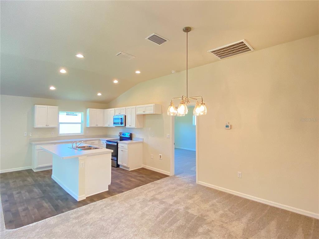 A kitchen with white cabinets and a center island opens to a carpeted dining area — 8190 N WAKEFIELD DRIVE, CITRUS SPRINGS, FL