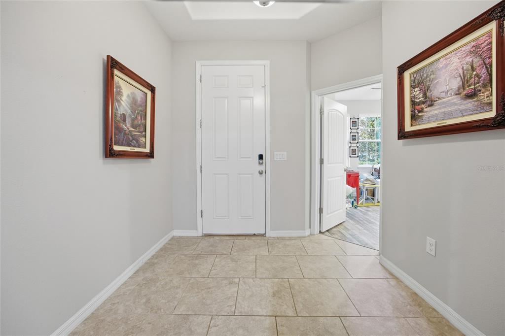 A tiled entryway features a white front door, two framed landscape paintings, and an open doorway — 5626 SW 50TH COURT, OCALA, FL