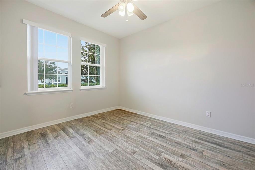 An empty bedroom features light gray walls, wood-look tile flooring, two windows, and a ceiling fan — 5626 SW 50TH COURT, OCALA, FL