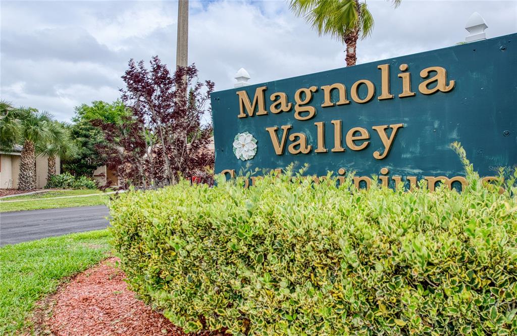 A green sign for Magnolia Valley Condominiums stands behind a manicured hedge — 7040 COGNAC DRIVE UNIT 3, NEW PORT RICHEY, FL