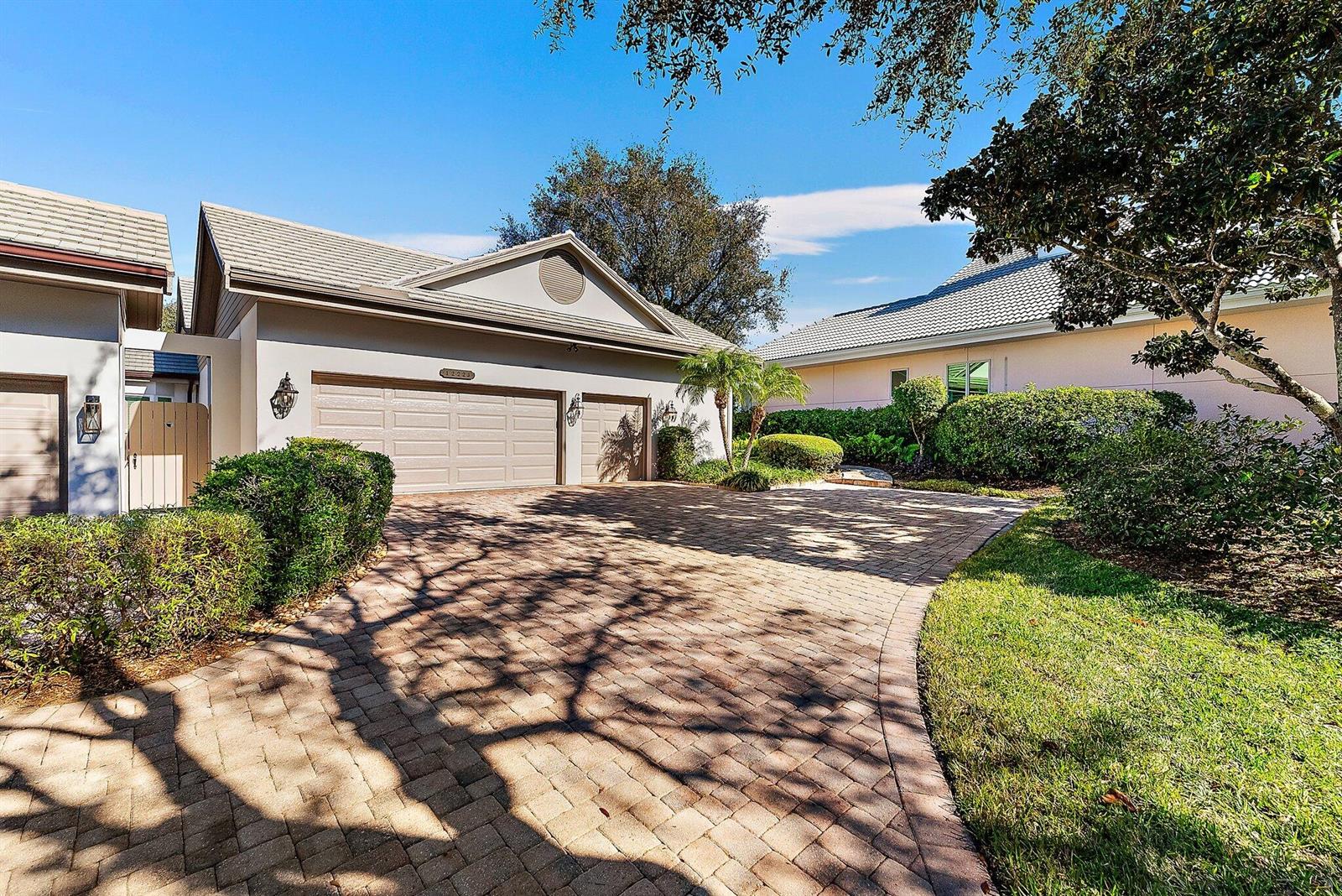A paved driveway leads to the three-car garage of a suburban house with landscaping — 12223 SE Birkdale Run, Jupiter FL 33469, JUPITER, FL