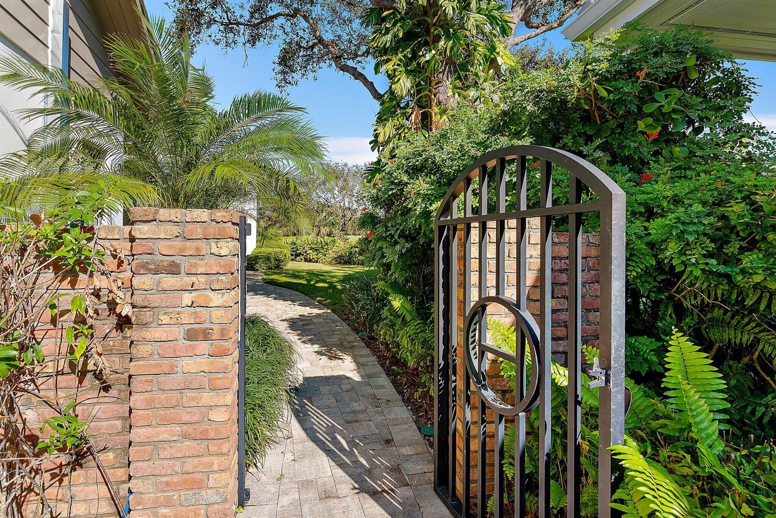 A brick wall and a black metal gate open to a stone walkway outdoors — 12223 SE Birkdale Run, Jupiter FL 33469, JUPITER, FL
