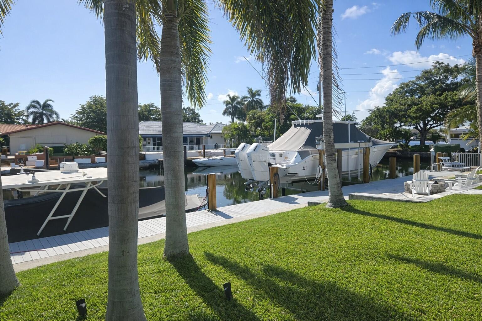 A waterfront backyard features a green lawn, palm trees, a dock, and two moored boats — 3910 NE 26th Avenue, Lighthouse Point FL 33064, LIGHTHOUSE POINT, FL