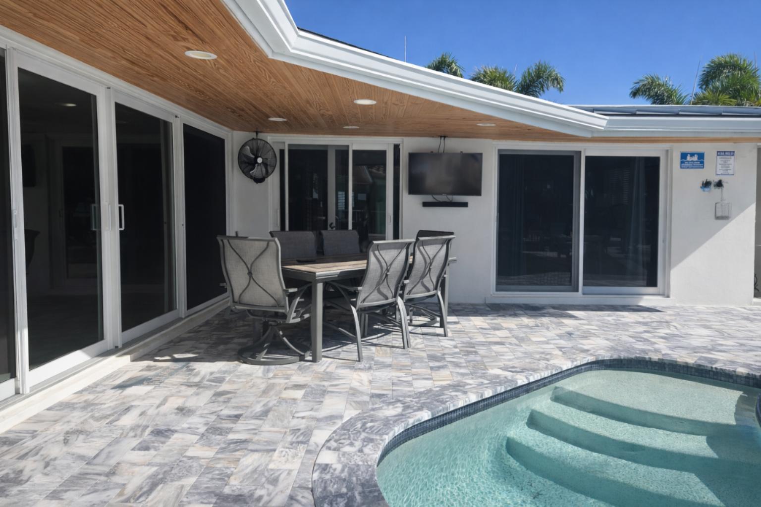 A patio with a dining set, pool, and wall-mounted television under a wood-paneled ceiling — 3910 NE 26th Avenue, Lighthouse Point FL 33064, LIGHTHOUSE POINT, FL