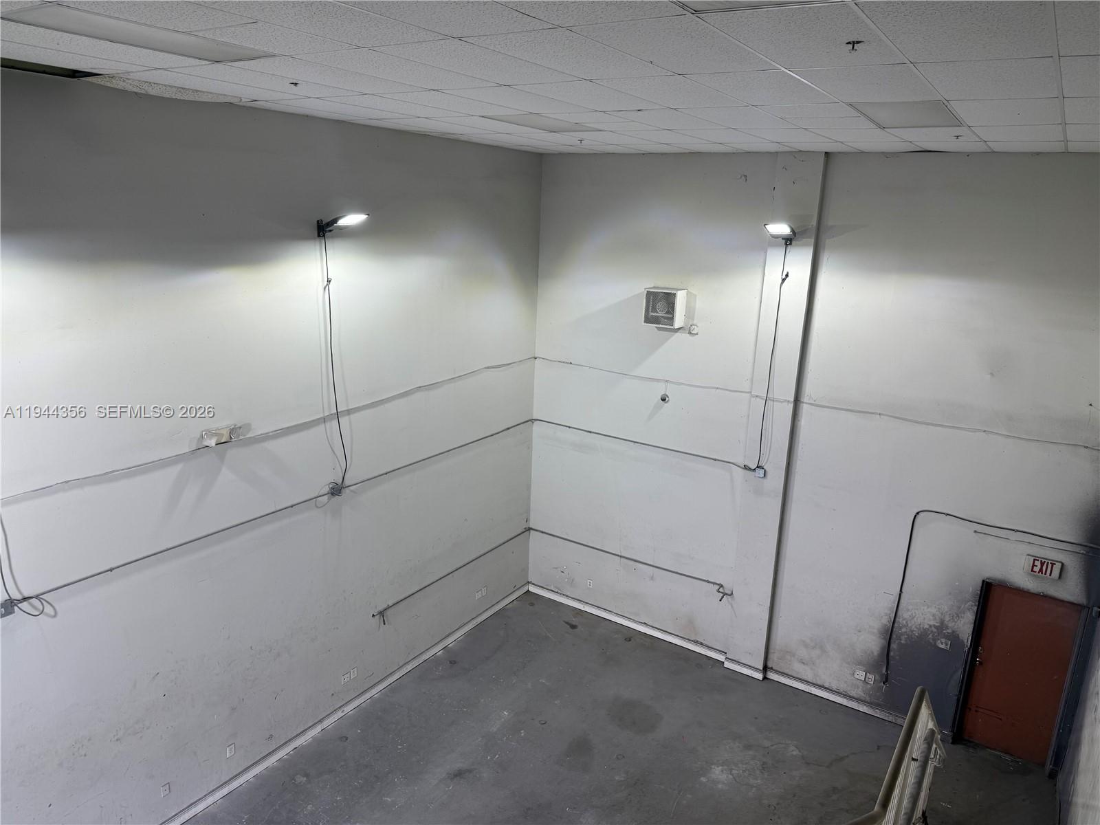 An interior view of a high-ceilinged industrial space with concrete floors and two wall-mounted lights — 16723 SW 117th Ave # 6F, Miami FL 33177, MIAMI, FL
