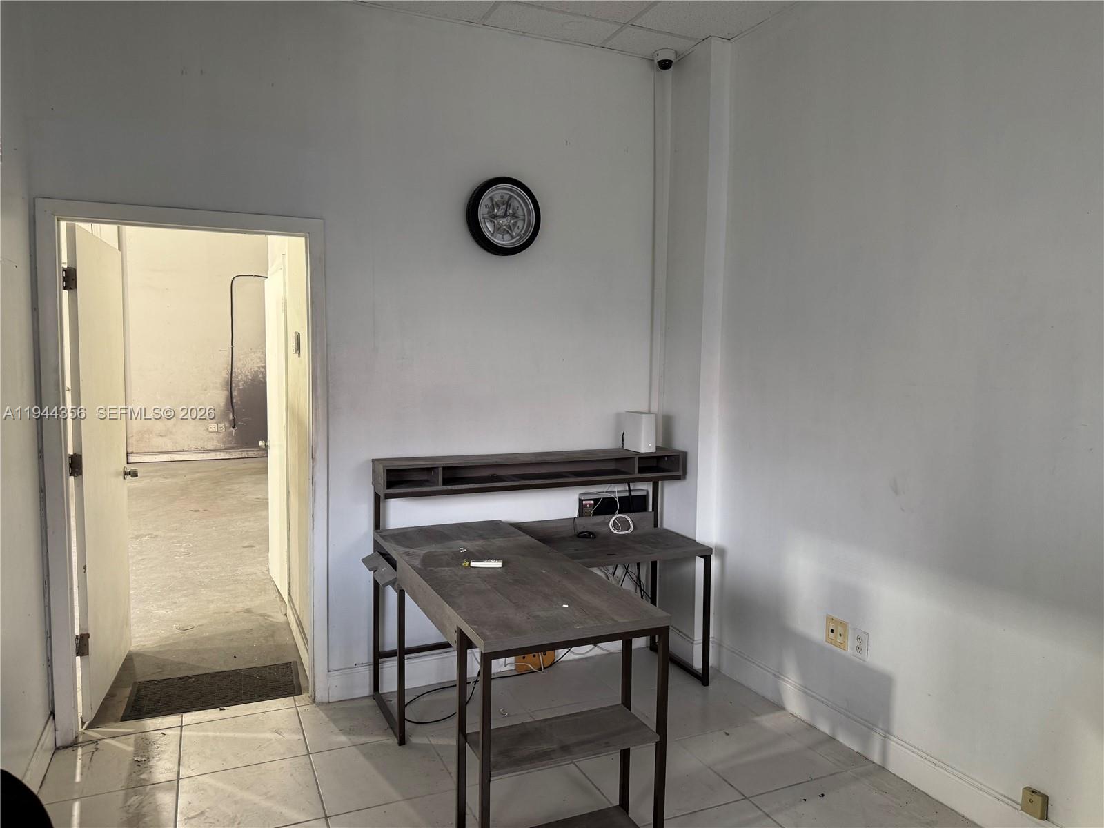 A small office space features a grey desk, a wall clock, and an open doorway — 16723 SW 117th Ave # 6F, Miami FL 33177, MIAMI, FL