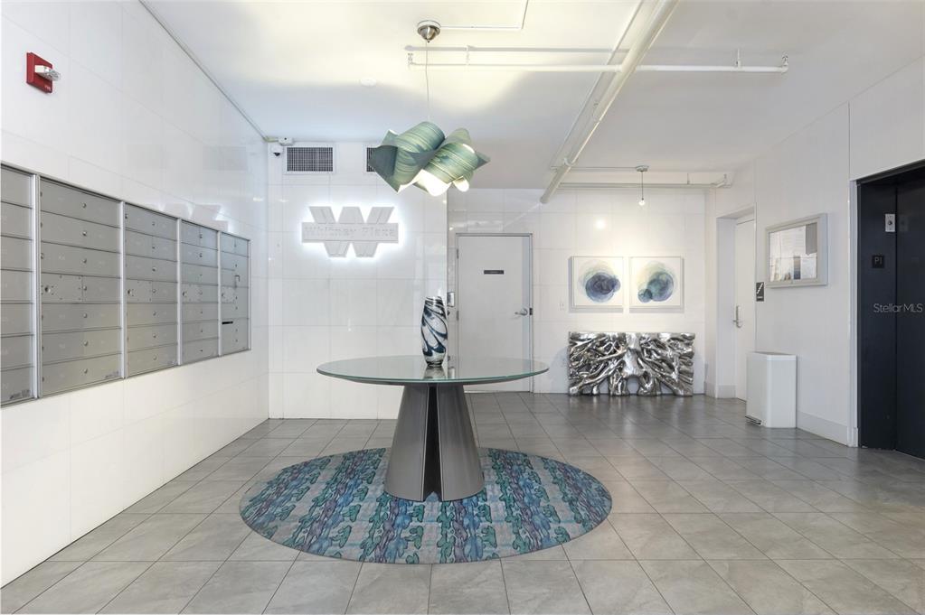 A modern building lobby features a glass-topped table, mailboxes, and a unique sculptural light fixture — 226 5TH AVENUE N UNIT M02, ST PETERSBURG, FL