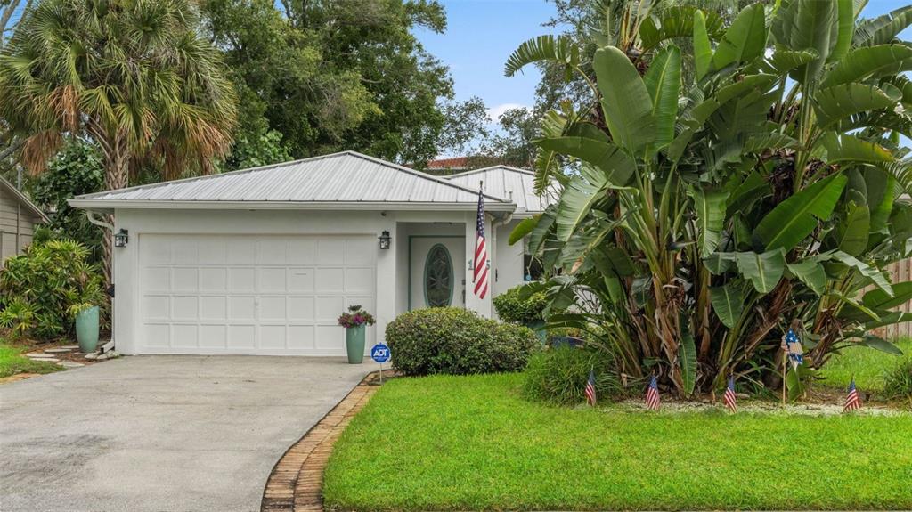 A single-story house with a white garage, metal roof, and large tropical plants in front — 105 ADALIA AVENUE, TAMPA, FL