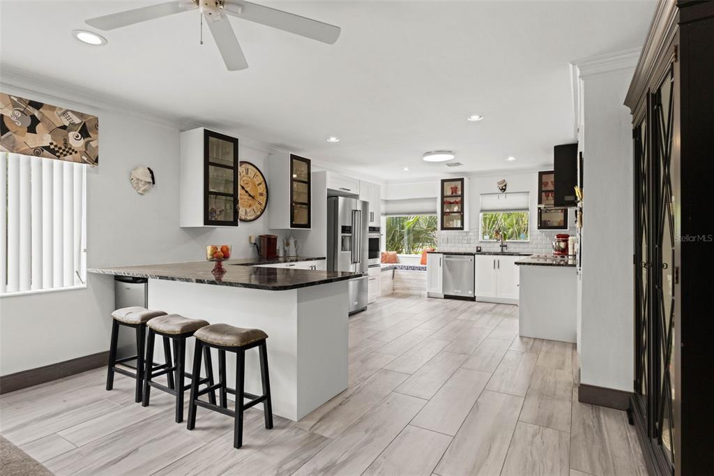 A kitchen with white cabinets, a dark countertop island, bar stools, and light wood-look flooring — 105 ADALIA AVENUE, TAMPA, FL