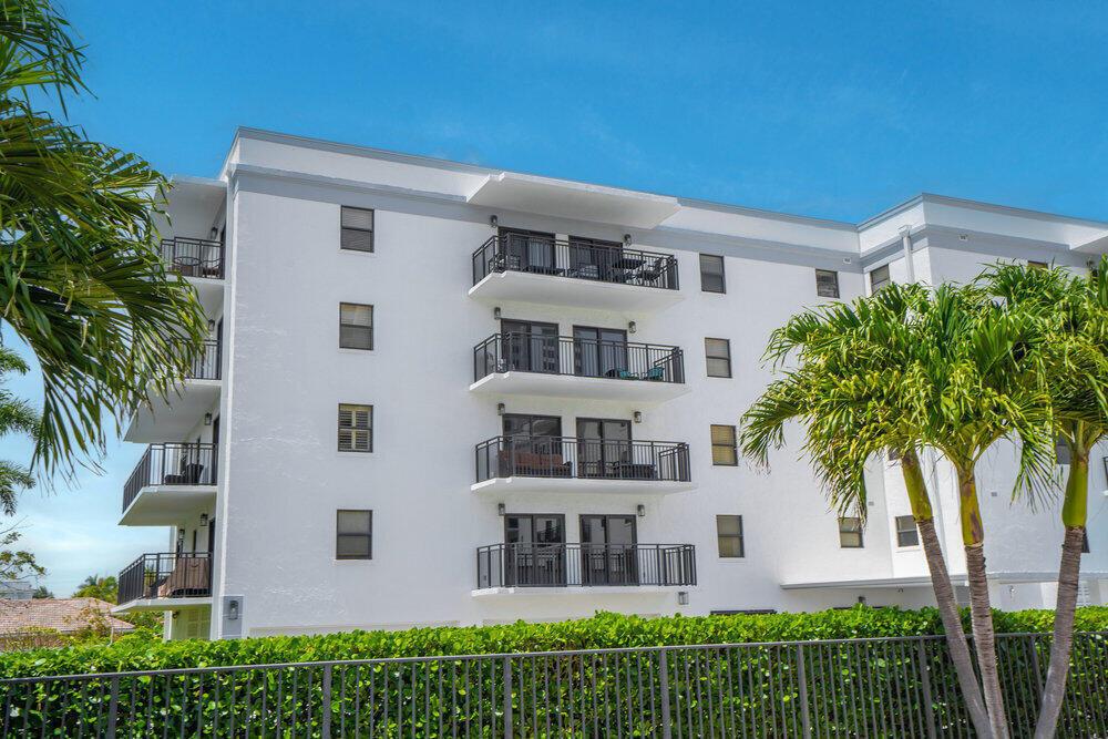A white four-story apartment building with balconies stands behind a green hedge and fence — 2679 S Ocean Boulevard # 31, Boca Raton FL 33432, BOCA RATON, FL