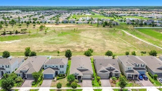 An aerial view shows a row of suburban houses bordering a large, undeveloped grassy field — 2427 ZABALLINA PLACE, DAVENPORT, FL