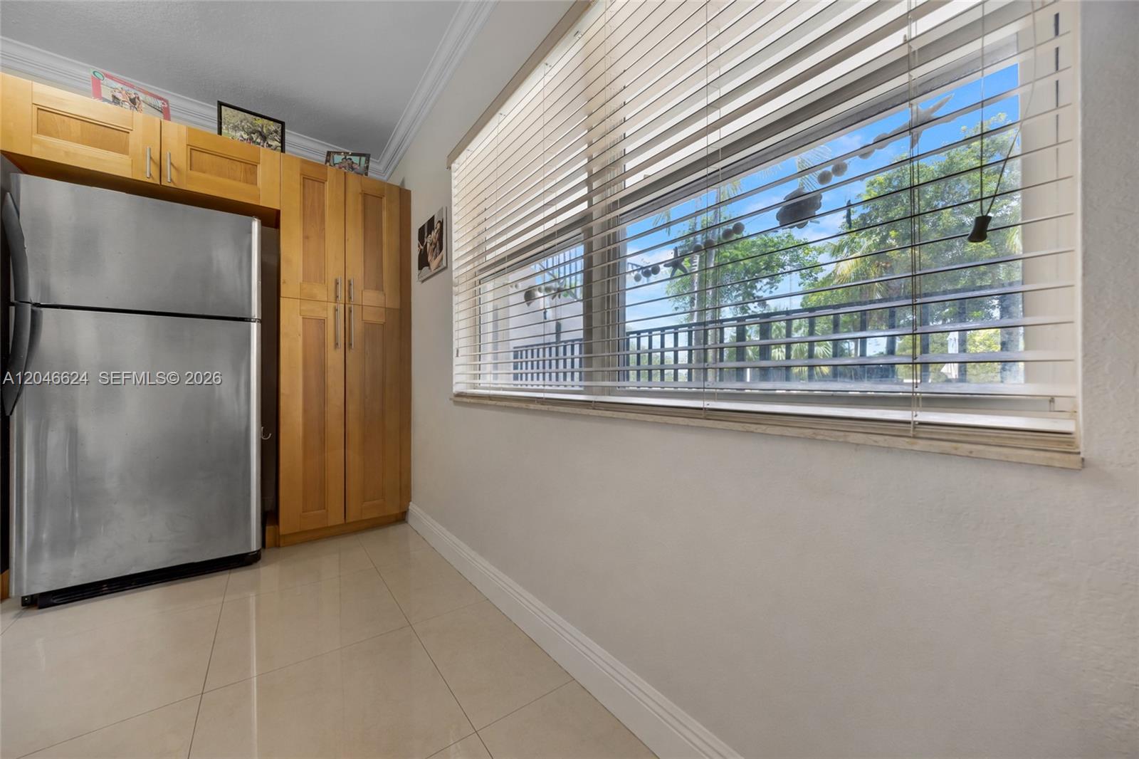 A stainless steel refrigerator sits next to wooden cabinets beside a window with blinds — FORT LAUDERDALE, FL