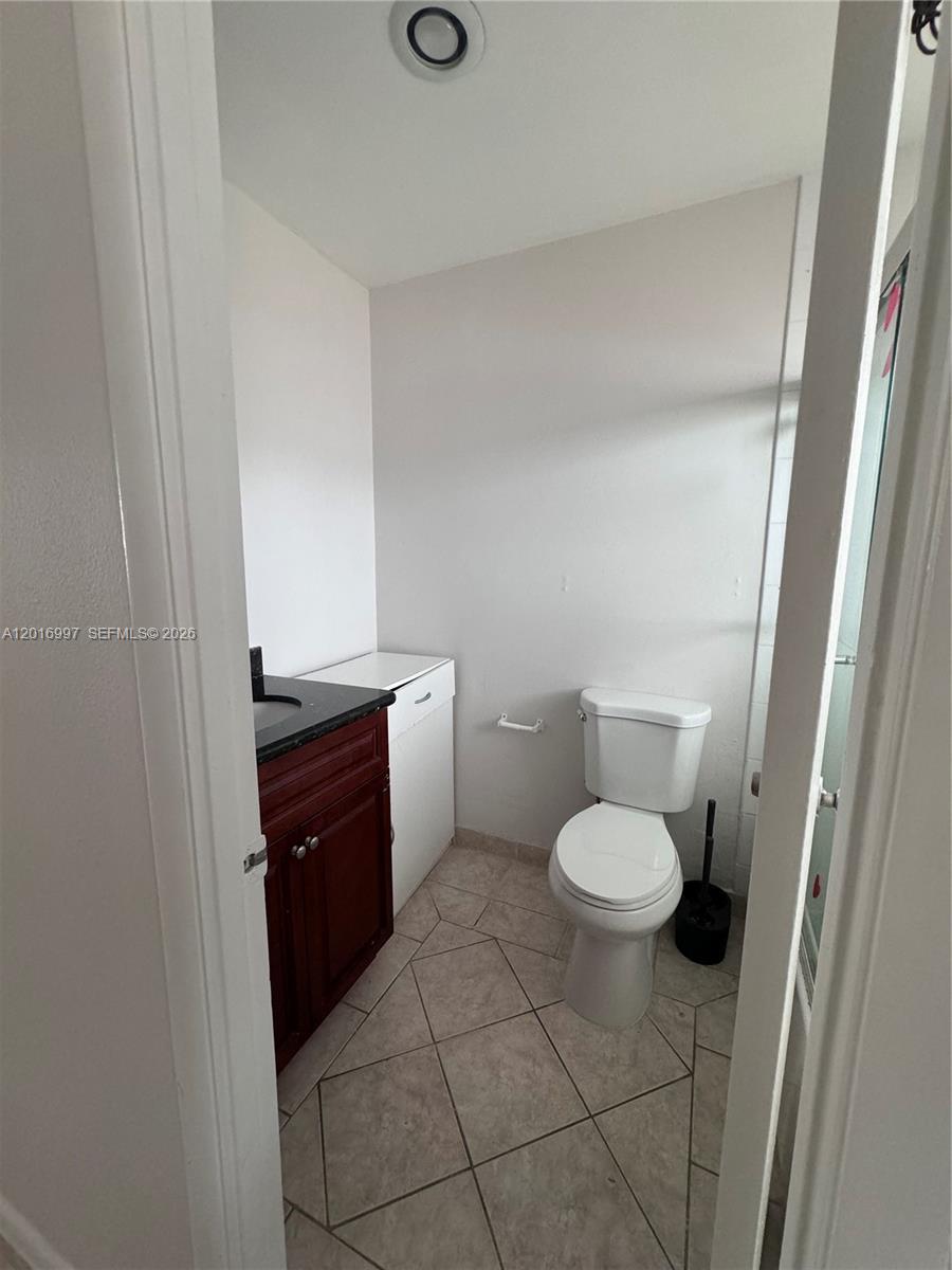 A small bathroom features a white toilet, a dark wood vanity, and light-colored floor tiles — 410 SE 2nd Ave # 21, Deerfield Beach FL 33441, DEERFIELD BEACH, FL