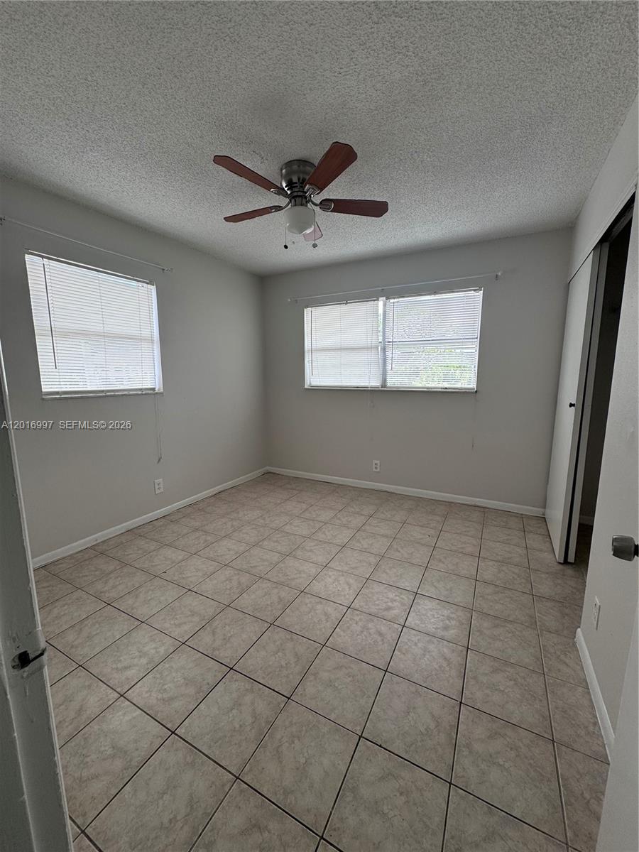 An empty bedroom features light-colored tile flooring, white walls, two windows, and a ceiling fan — 410 SE 2nd Ave # 21, Deerfield Beach FL 33441, DEERFIELD BEACH, FL