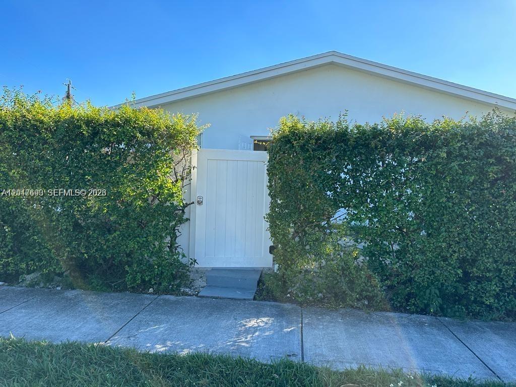 A white gate stands between tall green hedges in front of a house exterior — 301 9th St # 1, Hallandale Beach FL 33009, HALLANDALE BEACH, FL