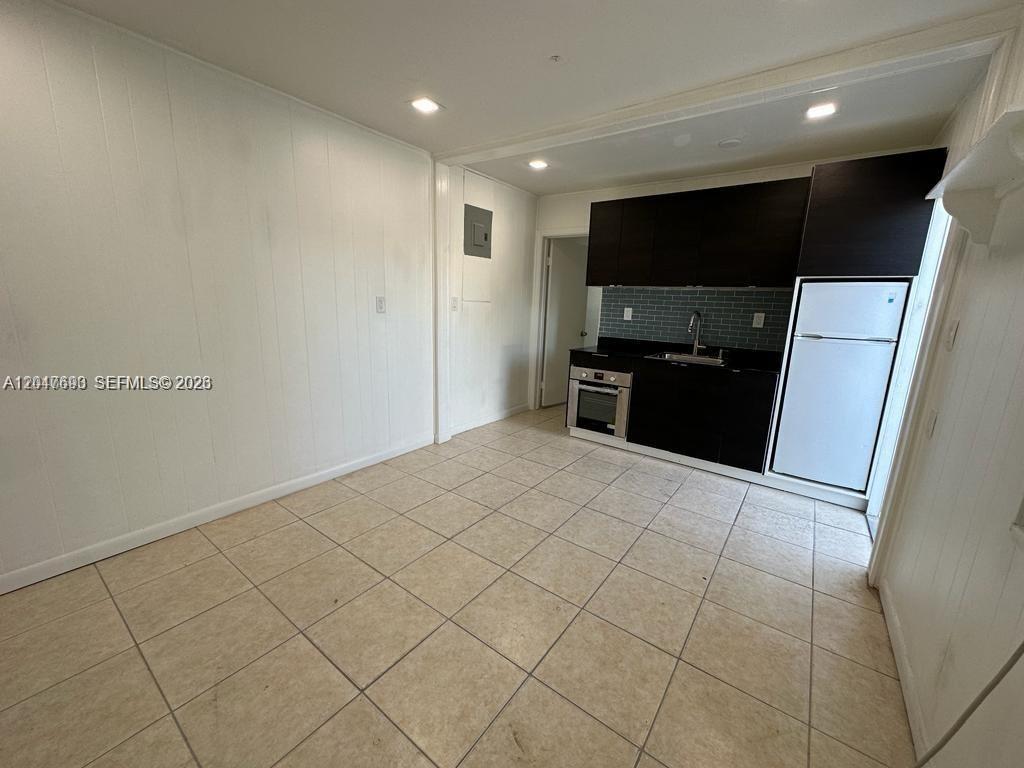 A kitchen features dark cabinets, a white refrigerator, and light-colored tile flooring — 301 9th St # 1, Hallandale Beach FL 33009, HALLANDALE BEACH, FL