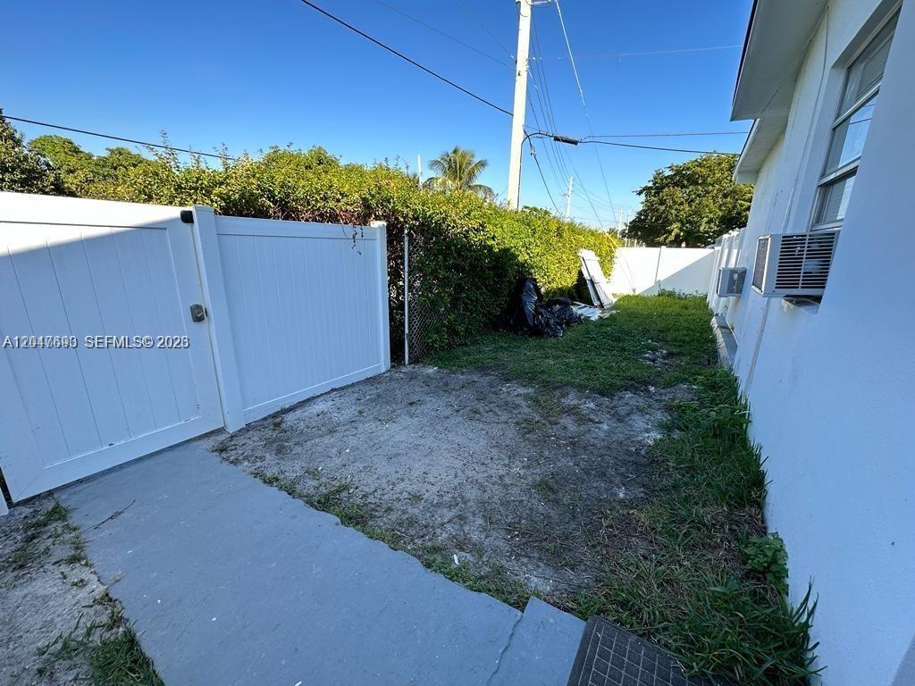 A white vinyl gate opens to a small, grassy side yard next to a building — 301 9th St # 1, Hallandale Beach FL 33009, HALLANDALE BEACH, FL