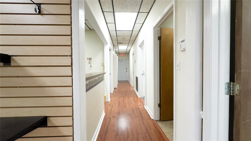 A hallway with wood-look flooring leads to a white door under a drop ceiling — 3612 5TH AVENUE N, ST PETERSBURG, FL