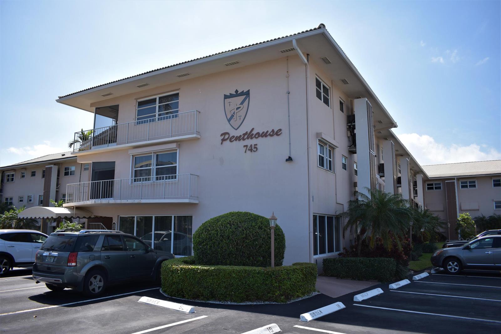 An exterior view of a multi-story apartment building with a parking lot in the foreground — 745 SE 19th Avenue # 112, Deerfield Beach FL 33441, DEERFIELD BEACH, FL