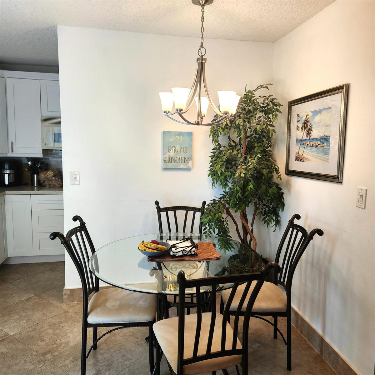 A dining area features a glass-topped table with four chairs under a chandelier — 745 SE 19th Avenue # 112, Deerfield Beach FL 33441, DEERFIELD BEACH, FL