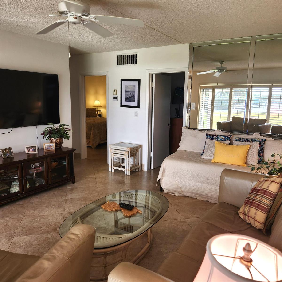 A living room features tile floors, a ceiling fan, a television, and a mirrored wall — 745 SE 19th Avenue # 112, Deerfield Beach FL 33441, DEERFIELD BEACH, FL