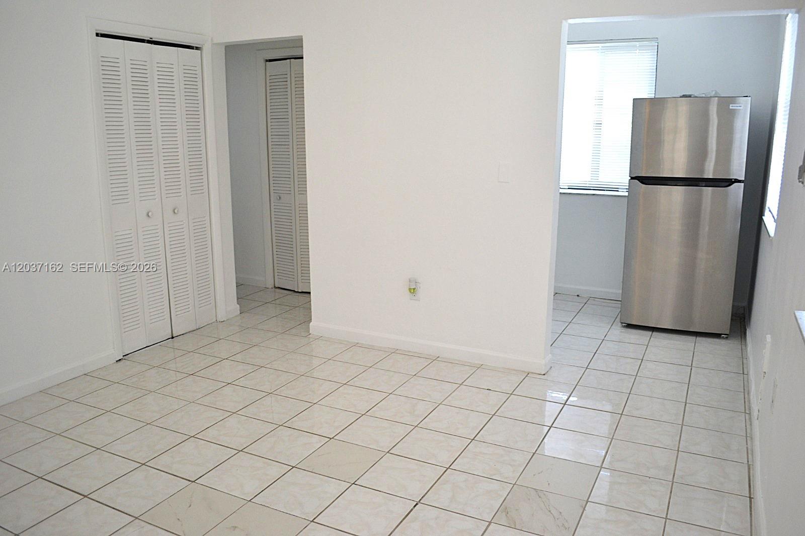 A room with white walls and tiled floors leads to a kitchen with a refrigerator — 1035 SW 4th St # 4, Miami FL 33130, MIAMI, FL