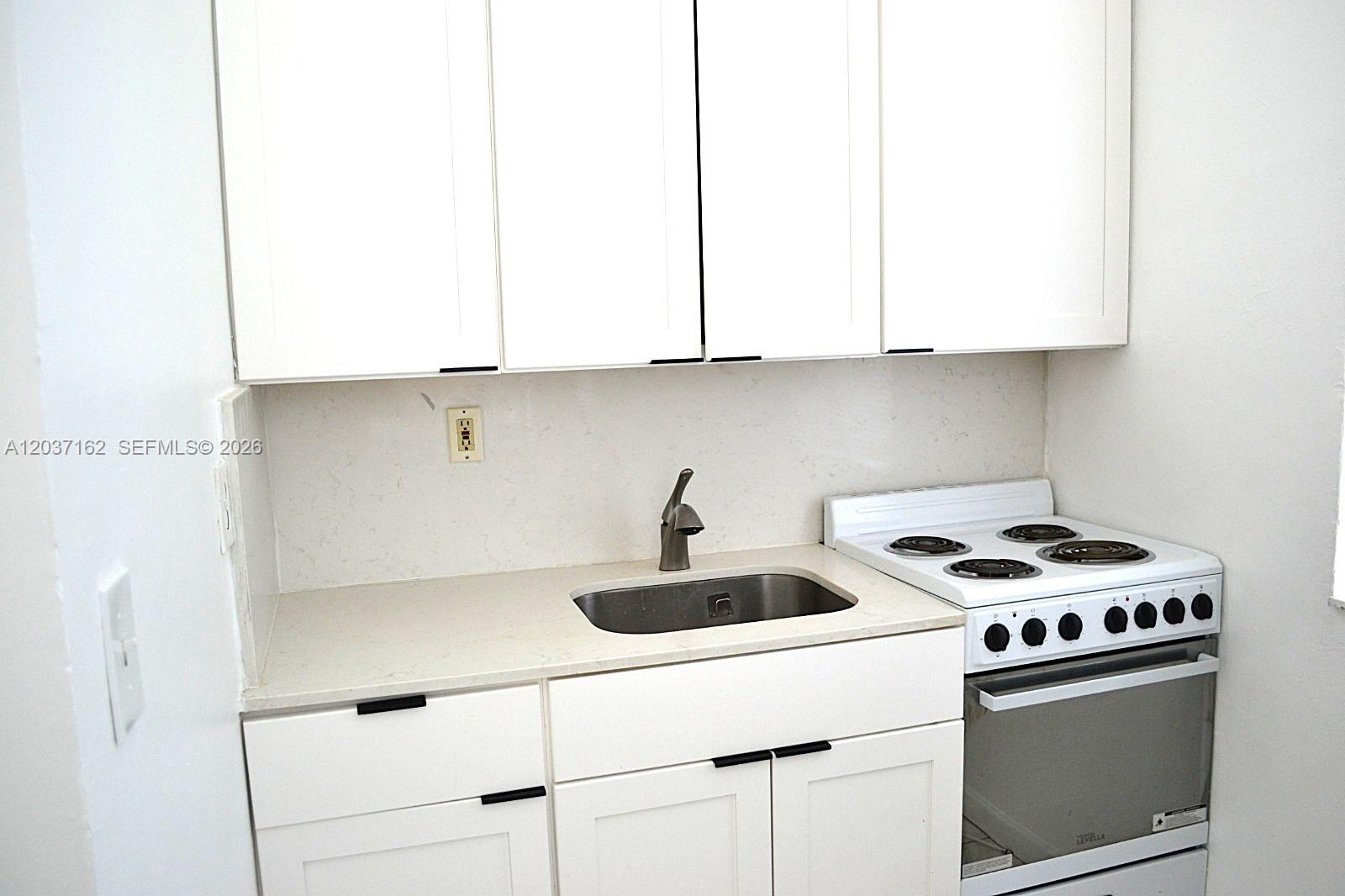 A small kitchen features white cabinets, a stainless steel sink, and a white electric stove — 1035 SW 4th St # 4, Miami FL 33130, MIAMI, FL