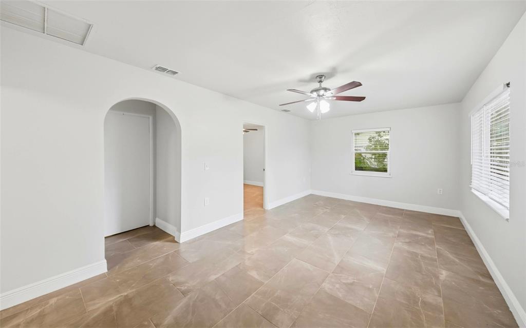 An empty room features light gray walls, large brown floor tiles, and an arched doorway — 1715 SUNSET DRIVE, LONGWOOD, FL