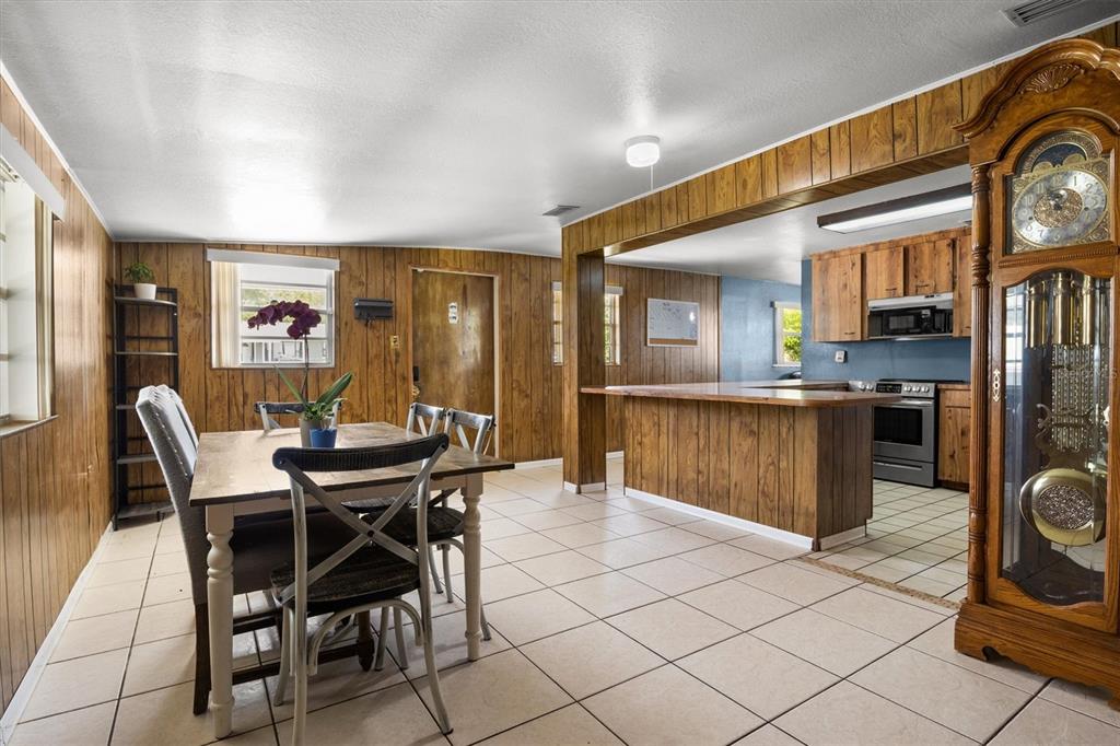 A dining area with wood-paneled walls and tile flooring opens into a kitchen with cabinets — 1307 MAYFLOWER DRIVE, LAKELAND, FL