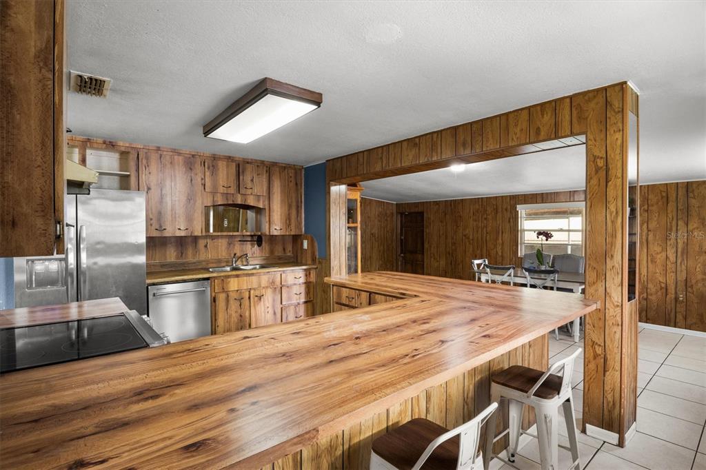 A kitchen with wood-paneled cabinets and walls, a large breakfast bar, and stainless steel appliances — 1307 MAYFLOWER DRIVE, LAKELAND, FL