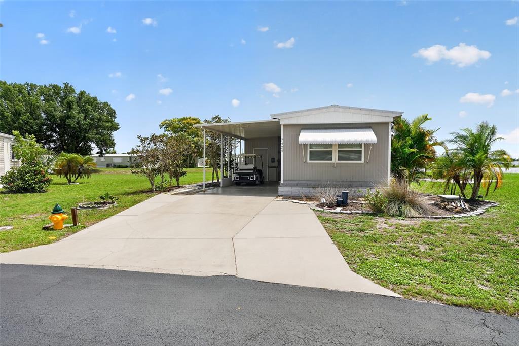 A single-story manufactured home features a concrete driveway, a covered carport, and a golf cart — 7424 WIDNESS LANE, PORT CHARLOTTE, FL