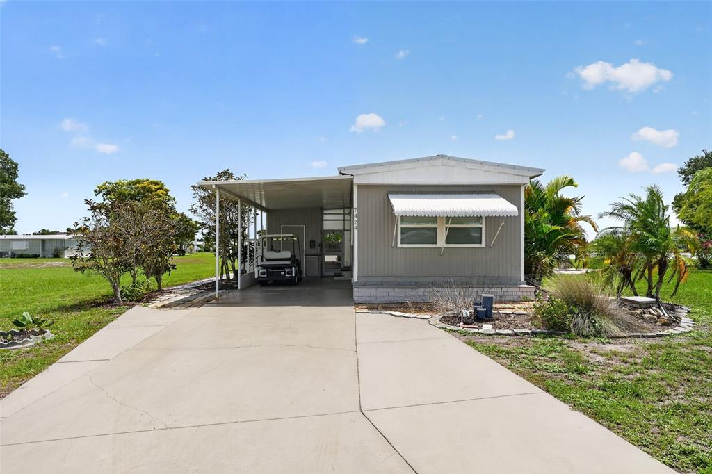 A single-story manufactured home features a concrete driveway, a carport, and a golf cart — 7424 WIDNESS LANE, PORT CHARLOTTE, FL