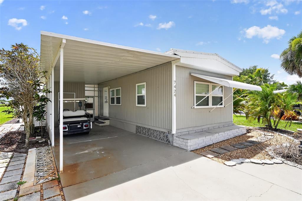 A single-story manufactured home with a carport and a golf cart parked underneath — 7424 WIDNESS LANE, PORT CHARLOTTE, FL