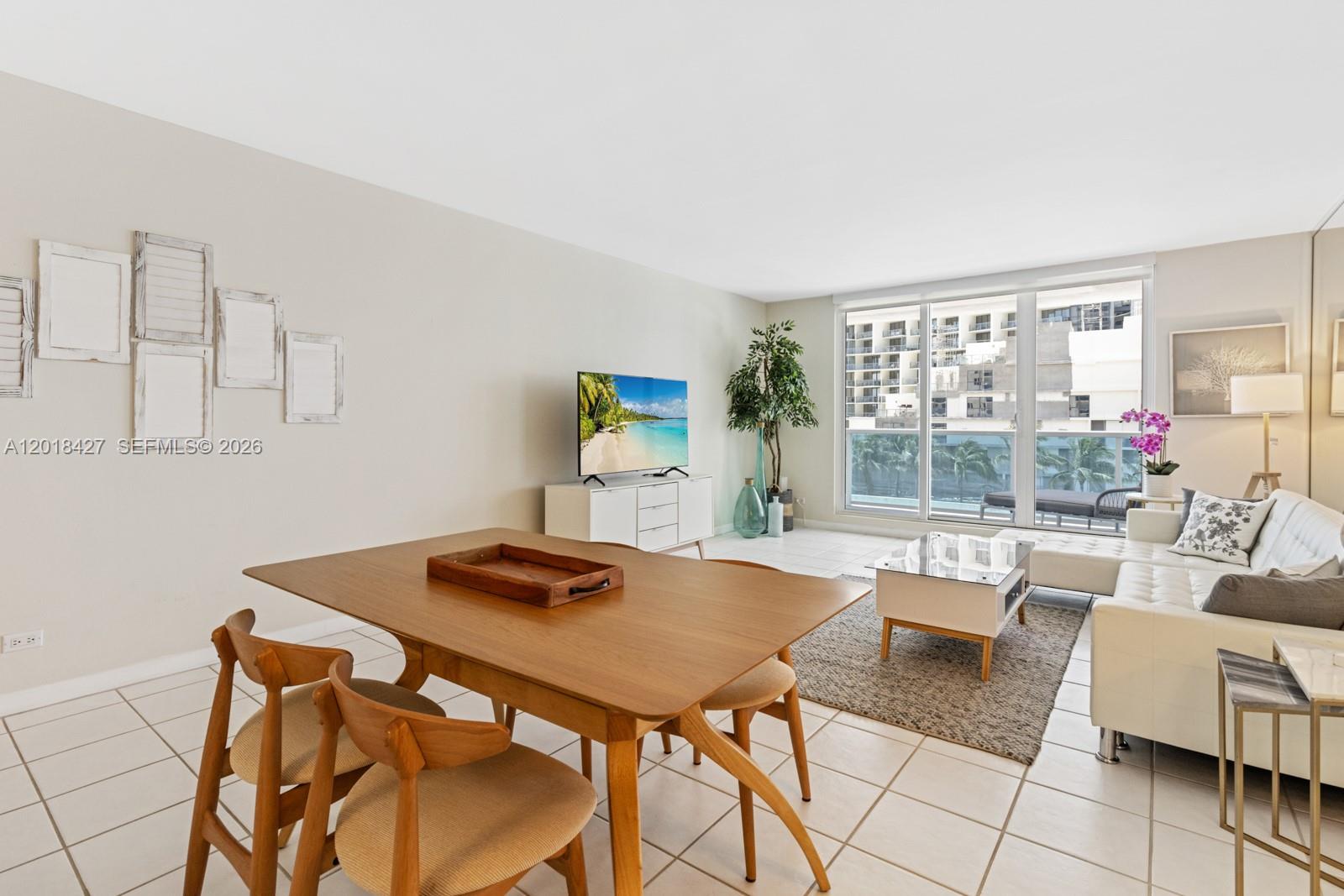 A living and dining area features white tile floors, a wooden table, and a balcony view — 2301 Collins Ave # 404, Miami Beach FL 33139, MIAMI BEACH, FL