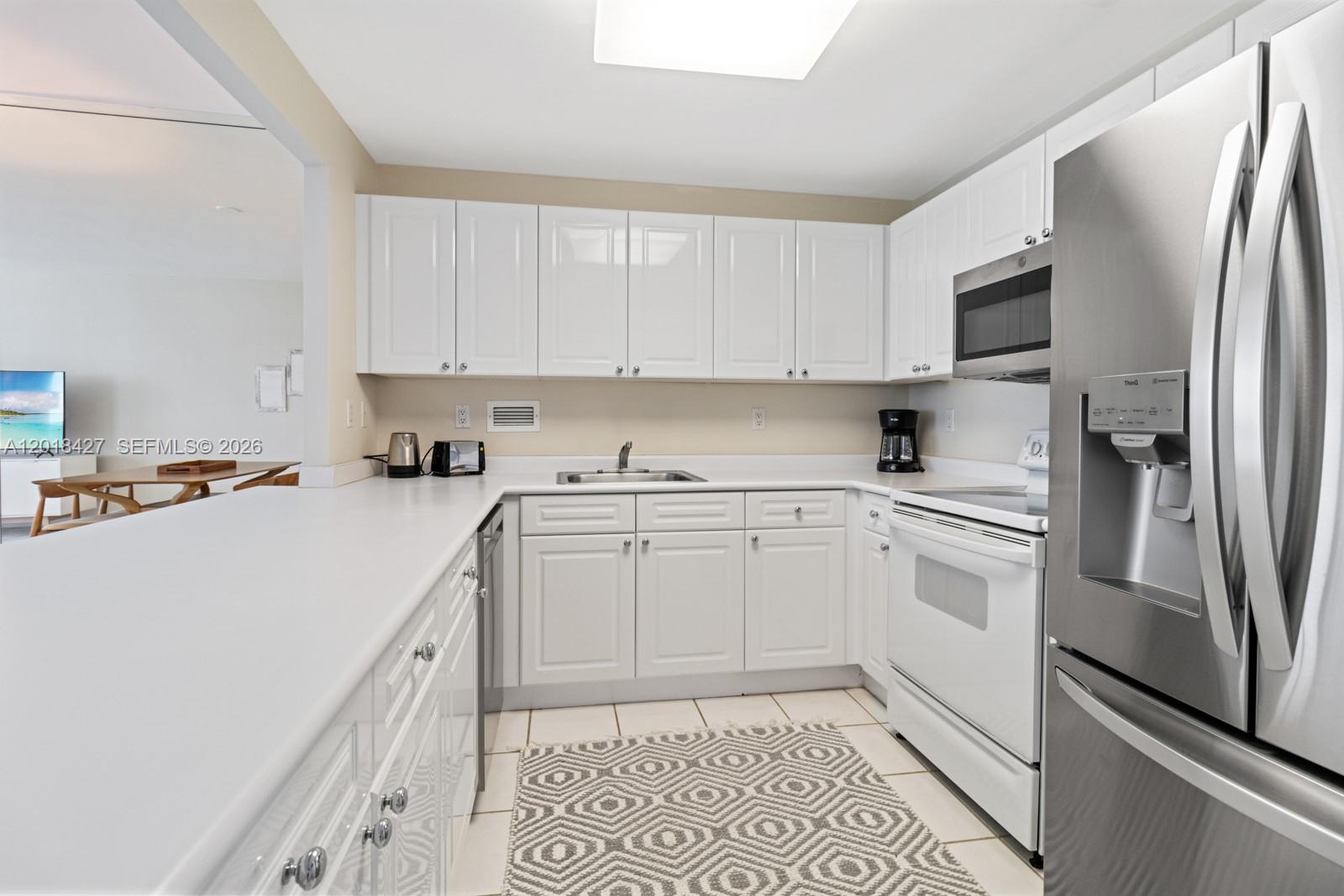 A kitchen features white cabinets, stainless steel appliances, and a patterned rug on tile floors — 2301 Collins Ave # 404, Miami Beach FL 33139, MIAMI BEACH, FL